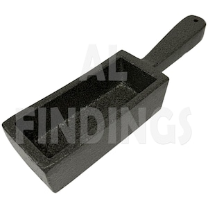 Puede incluir: Un molde de hierro fundido negro con un mango para hacer barras rectangulares de metal. El molde tiene una superficie texturizada.