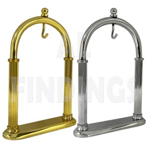 May include: Two decorative stands for displaying watches. The stand on the left is gold and the stand on the right is silver. Both stands have a hook on top and a base with a fluted design.