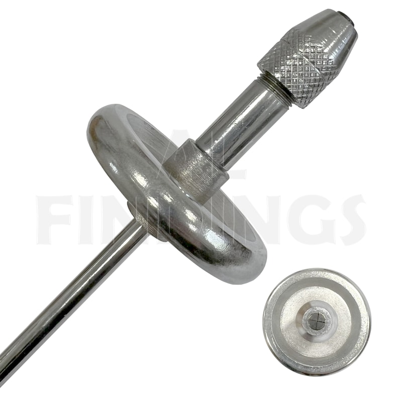 May include: A silver metal drill chuck with a rotating handle and a long, thin shaft. The chuck is designed to hold small drill bits for precise work.