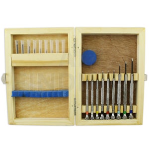 Peut inclure: Un coffret en bois contenant divers petits outils. Le côté gauche contient des aiguilles et des tubes, tandis que le côté droit présente un ensemble de tournevis de précision avec des manches colorés. La boîte est en bois clair.