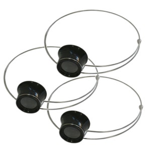 May include: Two black magnifying glasses with silver headbands. The magnifying glasses are attached to the headbands with a silver hinge.
