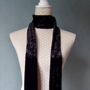May include: A black velvet scarf displayed on a mannequin. The scarf is long and slender, with a soft, textured finish. The mannequin is cream-coloured with a white top and a pattern of small hearts.
