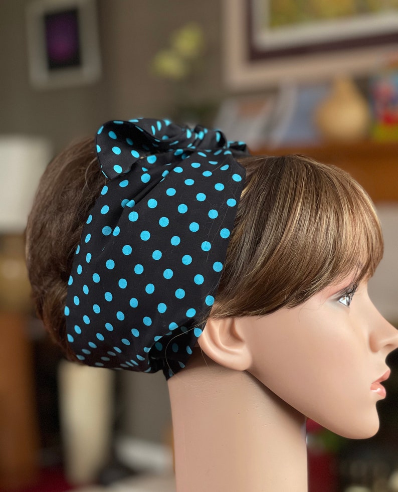 Peut inclure: Un bandeau noir &agrave; pois bleus est nou&eacute; sur la t&ecirc;te d'un mannequin. Le bandeau est en tissu et pr&eacute;sente un motif r&eacute;p&eacute;titif de pois bleu clair sur fond noir. Le bandeau est nou&eacute; en forme de n&oelig;ud sur le dessus de la t&ecirc;te.
