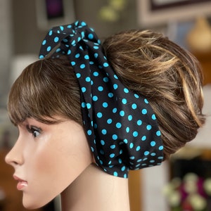 Peut inclure: Un foulard noir &agrave; pois bleu clair nou&eacute; en n&oelig;ud. Le foulard est enroul&eacute; autour d'une t&ecirc;te de mannequin avec des cheveux bruns. Le foulard est un accessoire r&eacute;tro.