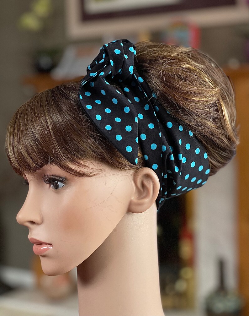 Peut inclure: Un foulard noir &agrave; pois bleu clair est nou&eacute; autour de la t&ecirc;te d'un mannequin. Le foulard est nou&eacute; sur le dessus, mettant en valeur le motif. Le mannequin a les cheveux bruns et est vu de profil.