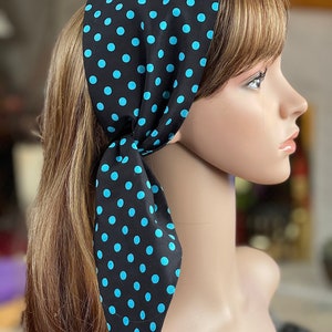 Peut inclure: Un foulard noir orn&eacute; de pois bleu clair. Le foulard est nou&eacute; &agrave; la nuque, les extr&eacute;mit&eacute;s pendantes. Le foulard est pr&eacute;sent&eacute; sur une t&ecirc;te de mannequin avec des cheveux ch&acirc;tain clair.