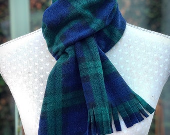 May include: A blue and green plaid scarf with fringed ends is draped over a mannequin. The scarf is made of a soft material and features a classic plaid pattern. The scarf is a winter accessory.