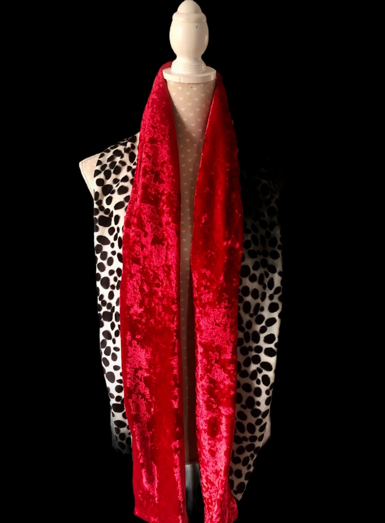 May include: A vibrant red velvet scarf draped over a mannequin. The scarf's texture is visible, and it contrasts with the black and white spotted fabric behind it. The scarf is a fashion accessory.