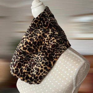 Könnte beinhalten: Ein Schal mit Leopardenmuster. Der Schal besteht aus einem weichen, plüschigen Material mit einem Muster aus schwarzen und braunen Flecken auf beigem Hintergrund. Der Schal ist über eine Schaufensterpuppe drapiert.
