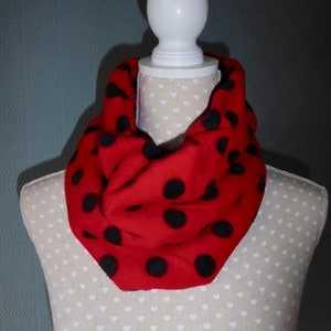 Pode incluir: Cachecol vermelho com grandes bolinhas pretas. O cachecol é drapeado em volta da cabeça e ombros de um manequim branco. O cachecol é feito de um material macio e é um acessório de moda.