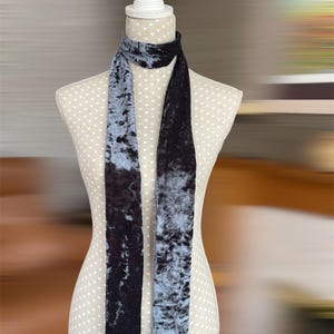 Könnte beinhalten: Ein langer Schal aus zerknittertem Samt, präsentiert auf einer Schaufensterpuppe. Der Schal hat ein zweifarbiges Design, eine Seite ist tiefschwarz, die andere ein gedämpftes Blau-Grau. Der Stoff hat eine weiche, strukturierte Oberfläche.