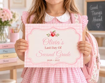 May include: A rectangular sign with a pink gingham border and a decorative frame. The text reads Olivia's Last Day Of Second Grade 2026 - 2027, featuring a small illustration of a red apple with a pink bow at the top center of the sign.