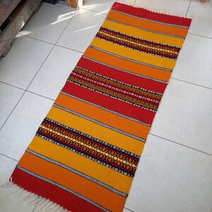 May include: A colorful woven rug with red, orange, and yellow stripes and a black geometric pattern. The rug has a fringe on the ends.