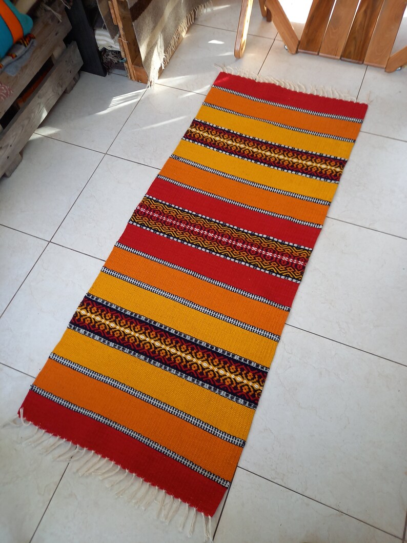 May include: A colorful woven rug with red, orange, and yellow stripes and a black geometric pattern. The rug has a fringe on the ends.
