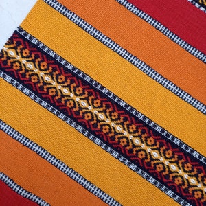 May include: A colorful woven table runner with a geometric pattern in shades of red, orange, yellow, and black.