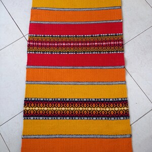 May include: A colorful woven rug with stripes of red, orange, and yellow. The rug has a geometric pattern in black and white.