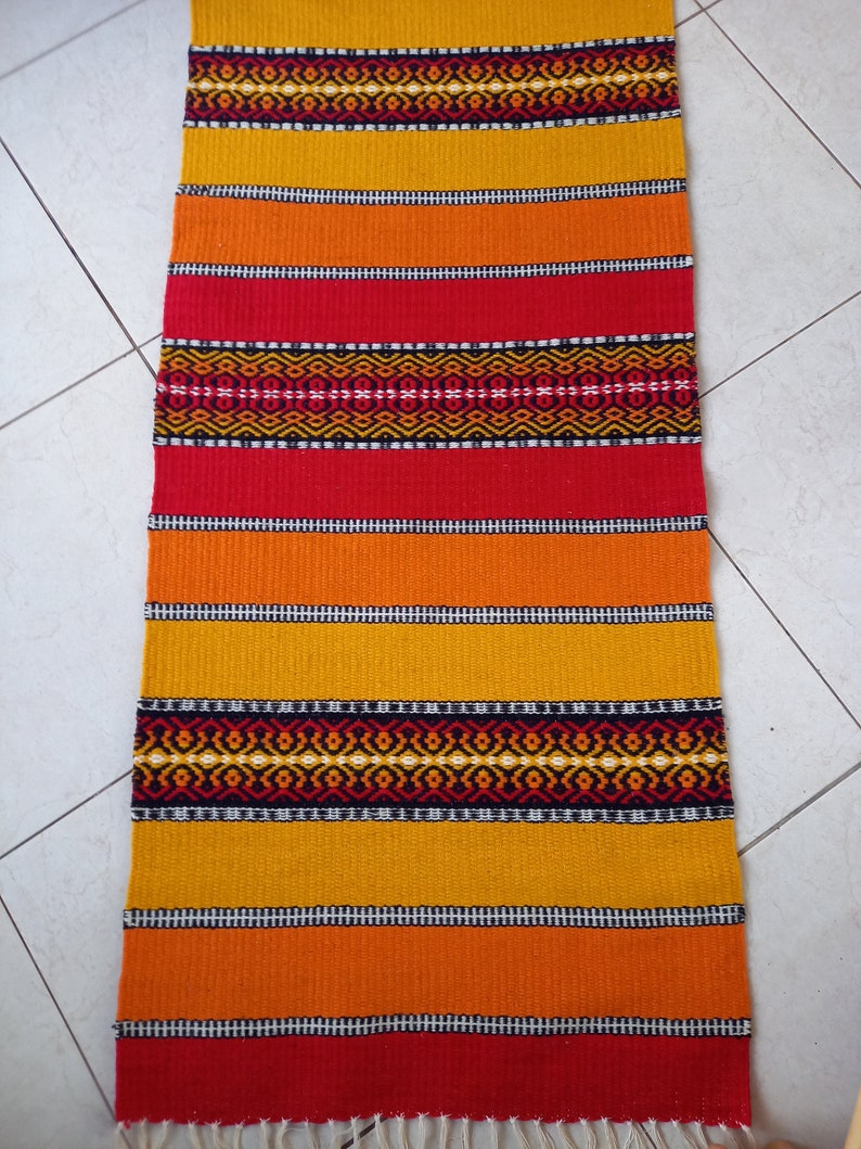 May include: A colorful woven rug with stripes of red, orange, and yellow. The rug has a geometric pattern in black and white.