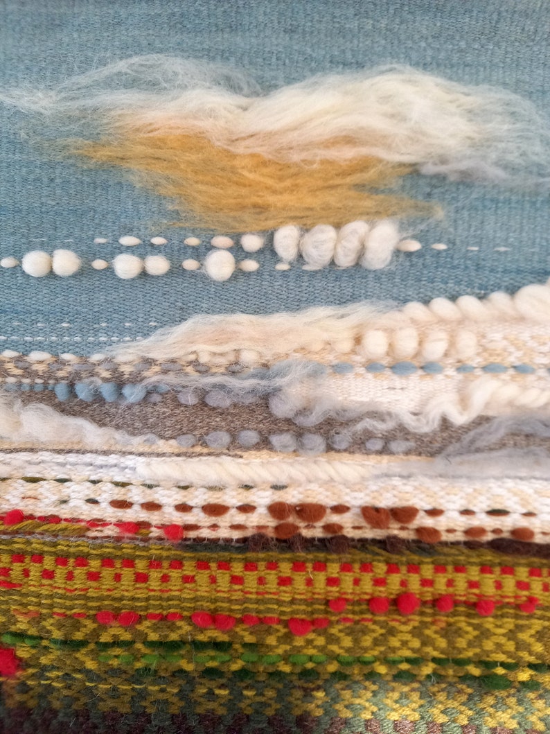 Puede incluir: Obra de arte textil con dise&ntilde;o de paisaje. Presenta un cielo azul claro con nubes blancas y amarillo dorado. Debajo, capas texturizadas de tejido en tonos verdes, rojos y marrones.