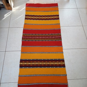 May include: A colorful woven rug with red, orange, and yellow stripes and black geometric patterns. The rug has a fringe on the bottom.