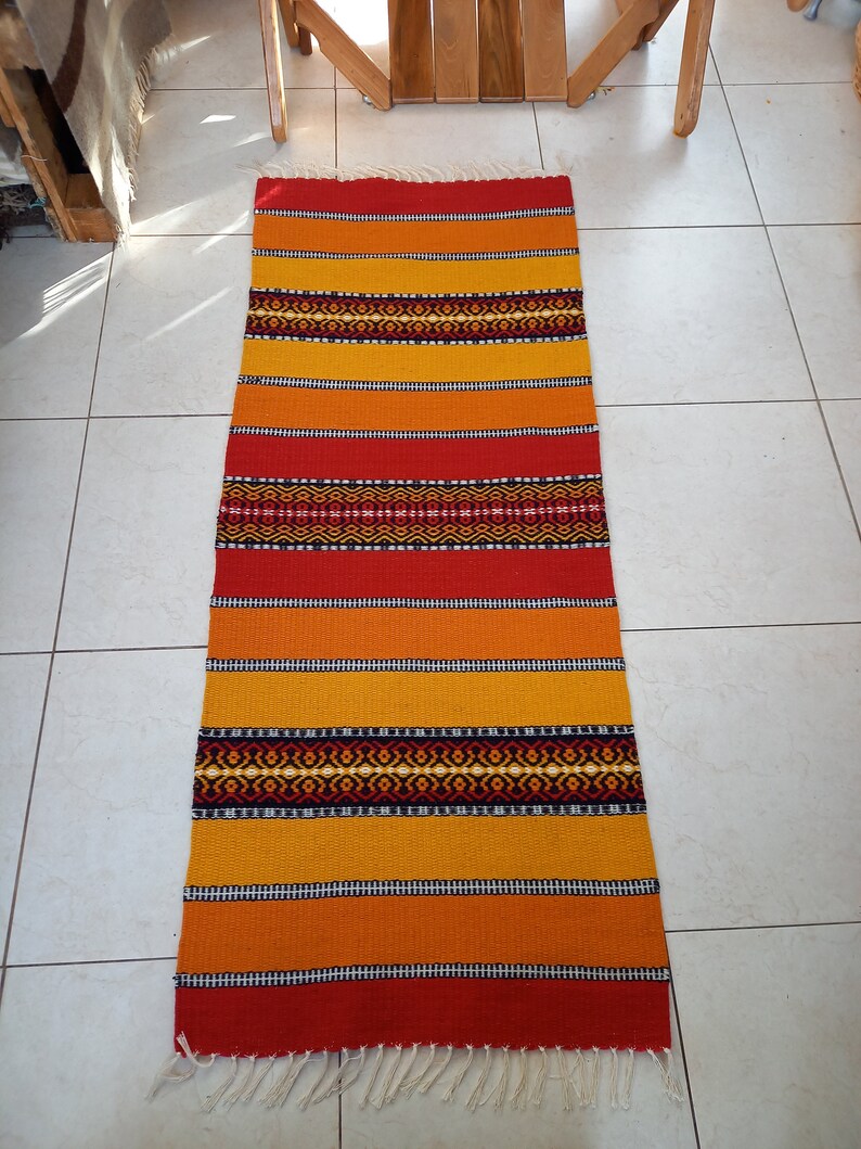 May include: A colorful woven rug with red, orange, and yellow stripes and black geometric patterns. The rug has a fringe on the bottom.