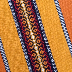 May include: A close-up of a woven fabric with a repeating geometric pattern in black, red, orange, and white. The fabric is a bright yellow color.