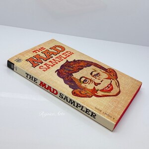 May include: A vintage paperback book titled "The Mad Sampler" with a colorful illustration of a grinning man's face on the cover.
