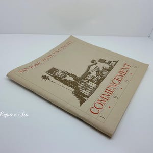 May include: A tan San Jose State University commencement program from 1986. The cover features dark brown text and a detailed line drawing of a campus building with a palm tree. The title reads San Jose State University Commencement 1986.