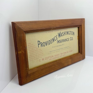 May include: A framed vintage insurance advertisement for Providence Washington Insurance Co. in Providence, Rhode Island. The ad lists various types of insurance coverage, including fire, marine, tornado, automobile, and more. The ad also includes the name and address of the agent, C.W. Cotton, in Waterloo, Iowa.