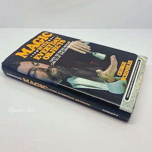 May include: A black and yellow book titled "Magic with Everyday Objects" by George Schindler. The book cover features a man performing a magic trick with a silver object.