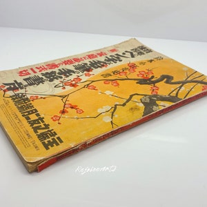 May include: A vintage Japanese book with a yellow cover featuring a black and white illustration of a tree with red blossoms. The text on the cover reads "昭和二十一年一月二十七日発行" and "第一巻".