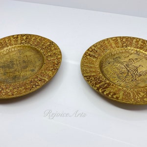 May include: Two small, round, brass plates with intricate designs. The plates feature a raised image of a building in the center, surrounded by a border of repeating patterns.