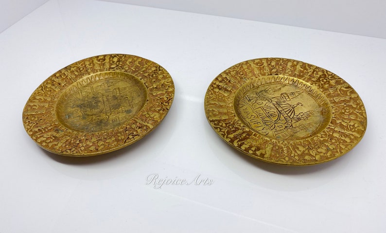 May include: Two small, round, brass plates with intricate designs. The plates feature a raised image of a building in the center, surrounded by a border of repeating patterns.