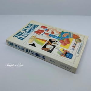 May include: A vintage paperback book titled "The Magic Handbook" by Peter Eldin. The cover features illustrations of various magic tricks, including a disappearing act, a card trick, and a cup and ball routine. The book is published by Simon and Schuster.