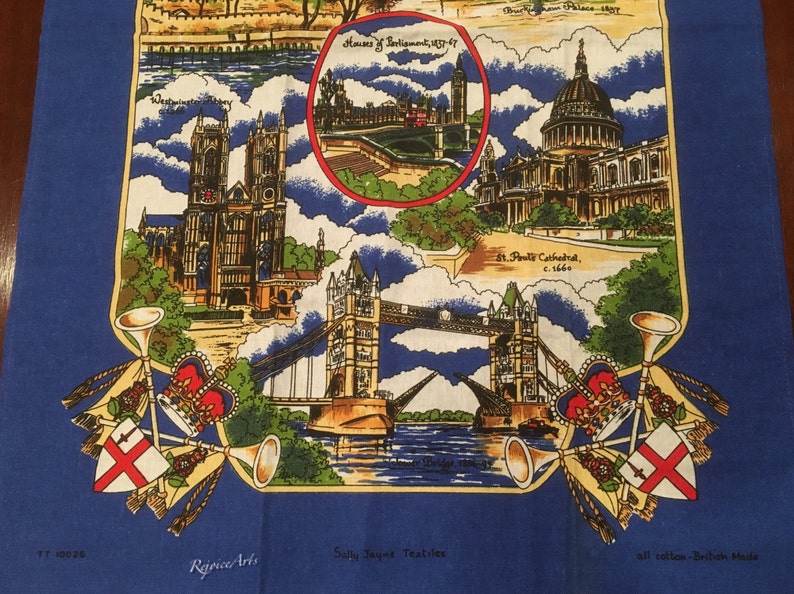 May include: A blue tea towel with a colorful illustration of famous London landmarks, including the Houses of Parliament, Tower Bridge, and St. Paul's Cathedral. The text "Houses of Parliament 1837-47", "St. Paul's Cathedral, c.1666", "Tower Bridge 1886-94", "Rejpice Arts", "Sally Jayne Textiles", and "all cotton - British Made" is printed on the towel.