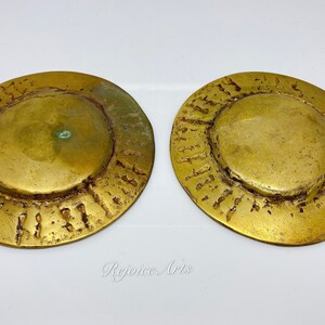 May include: Two round, gold-colored metal discs with a raised, textured rim and a smooth, slightly domed center. The discs are approximately 5 inches in diameter.