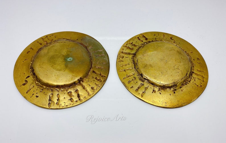 May include: Two round, gold-colored metal discs with a raised, textured rim and a smooth, slightly domed center. The discs are approximately 5 inches in diameter.