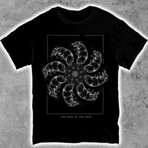 May include: Black t-shirt with a white graphic of rats in a circular design, with hands at the centre. The text "THE DRAW OF THE VOID" is printed below. The shirt is made of a soft material.