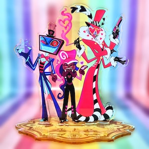 Może przedstawiać: Kolorowy akrylowy stojak z trzema postaciami z kreskówek. Postacie mają na sobie różne stroje, w tym czerwony płaszcz, czarny kombinezon i niebieski garnitur. Stojak ma złotą podstawę z dekoracyjnym wzorem i tęczowym tłem.