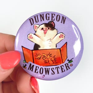 May include: A purple button featuring a white cat inside a red and orange box with the text "Dungeon Meowster".