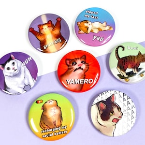 Puede incluir: Conjunto de 7 botones redondos de memes de gatos con diferentes expresiones de gatos y texto. Los botones son coloridos y presentan varios memes de gatos, incluyendo "recharging my social battery", "yap", "YAMERO", "Doei", "grote blij", "HUH", y "yipped my last".
