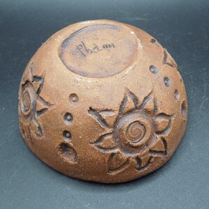 May include: A brown ceramic bowl with a sun design and the word "Phidan" inscribed on the bottom.