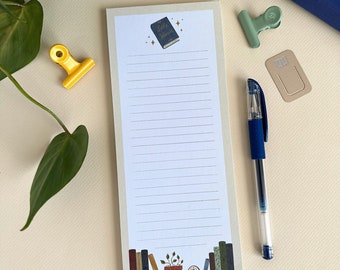 May include: A beige notepad with a lined white interior. The notepad has a graphic of a blue book with the text "Little Women" on the cover. The notepad also has a graphic of a potted plant and books at the bottom.