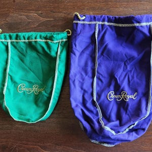 May include: Two drawstring bags with the Crown Royal logo. One bag is green and the other is purple.