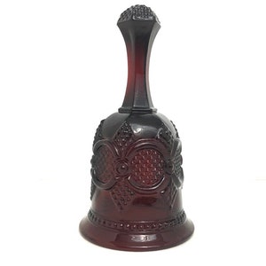 Puede incluir: Una campana de vidrio rojo oscuro con un patrón decorativo. La campana tiene una base ancha y un cuello estrecho.