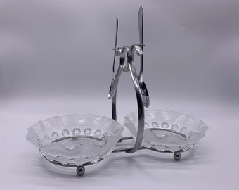 May include: A silver serving stand with two clear glass bowls. The stand has a decorative design and the bowls have a scalloped edge.