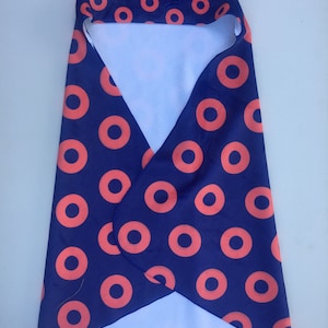 May include: A navy blue baby swaddle blanket with a hood, patterned with orange circles. The interior is a solid light blue. The blanket is folded and ready for use.
