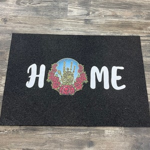 May include: Black doormat with the word "HOME" in white lettering and a colorful graphic of a hand with roses around it.