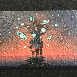 May include: A painting of a dark tree with a large, round, blue and green planet at its base. The tree is surrounded by smaller, round, blue and green planets with rings. The background is a gradient of orange, red, and purple.