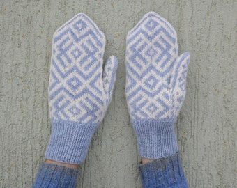 May include: A pair of knitted mittens in light blue and white. The mittens feature a geometric diamond pattern on the top and a ribbed cuff. The mittens are designed for warmth and style, perfect for cold weather.