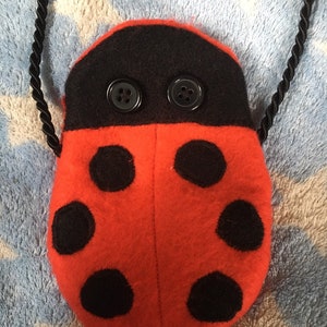May include: A red ladybug-shaped plush bag with black spots and black button eyes. The bag has a black cord handle.